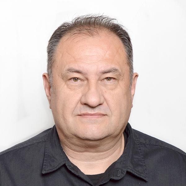 Man with short hair wearing a dark collared shirt against a plain background.