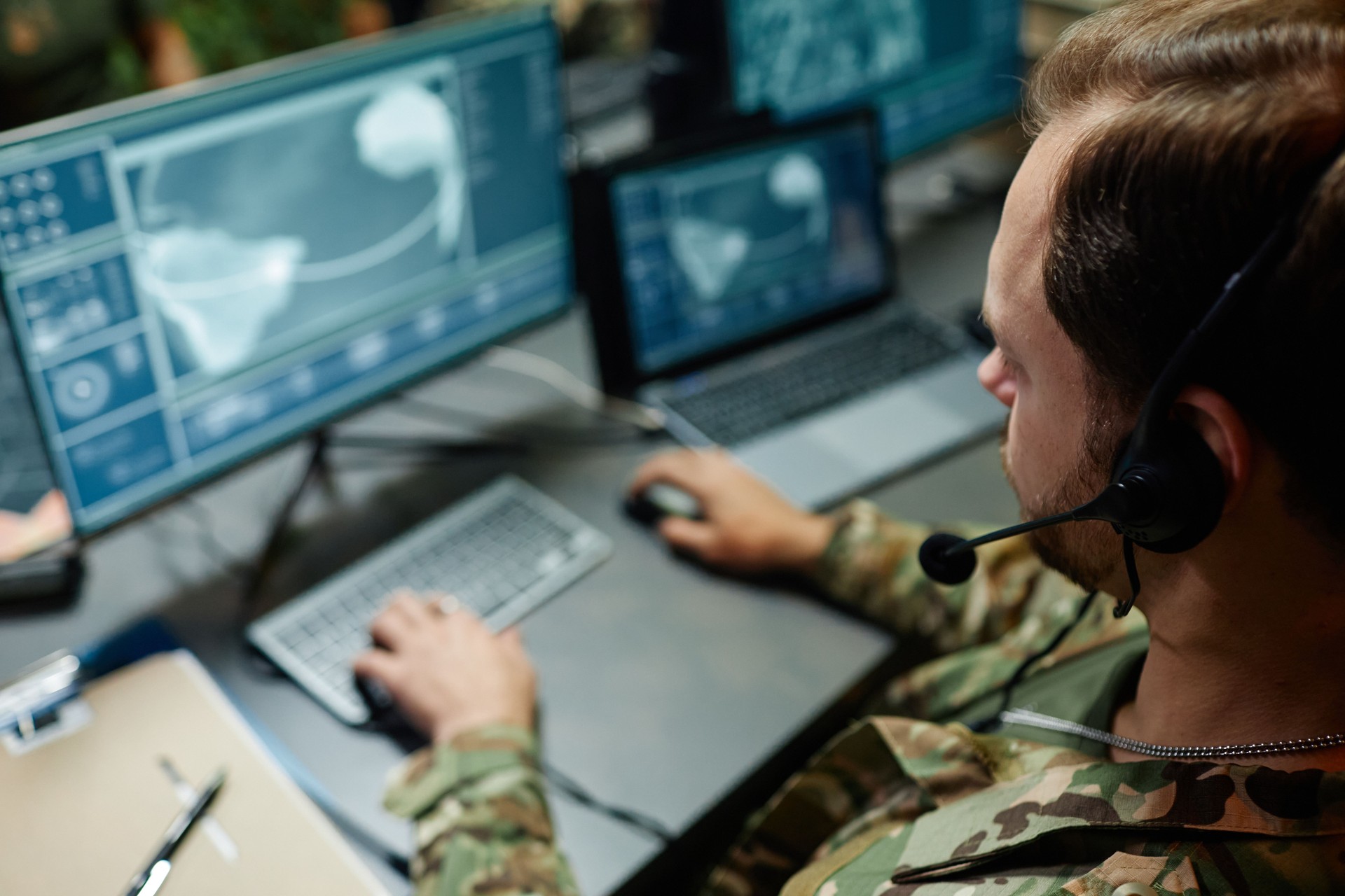 Focus on head of young military officer with headset sitting in front of screen